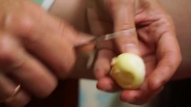 A woman cleans a small onion with a knife. Close-up.