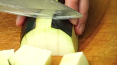 Cutting eggplant into slices on a wooden plank by a woman cook. Close-up