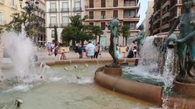 Valencia, İspanya; 08-02-2021: Valencia Meydanı 'ndaki çeşmenin 4k videosu (Fuente de las 8 acequias de Turia) turistler ve güvercinler tarafından çevrelenmiş su serinliyor.