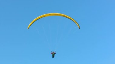 Paraşütle atlayan sporcu kadın büyük akbabalar tarafından kuşatılmıştı. Sanki aynı aileden geliyor gibiydiler. Arka planda muhteşem mavi bir gökyüzü vardı.