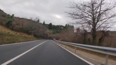 Sonbaharda El Bierzo bölgesinde, ıslak asfalt ile dağ yolunda ilerleyen ve arka planda tehlikeli virajları ve Cornatel kalesini alan bir arabanın sübjektif kamerasının 4K videosu.