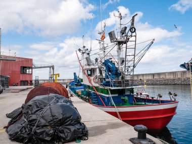 Laredo, Cantabria, İspanya; 08-17-2021: Kırmızı balıkçı teknesi Marina El Laredo binasının yanına yanaştı ve ağlar asfaltta toplanmaya ve gemiye yüklenmeye hazır.