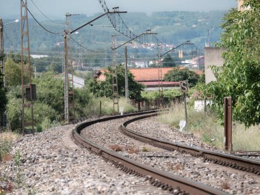 Tren raylarında güneşli ve sıcak bir günde Monforte de Lemos şehrinde evlerin ve bitkilerin yanında kaybolan kavisli tren yolu.