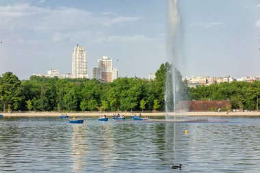Madrid, İspanya; 06-12-2022: Madrid 'deki La casa de campo gölünde kürek çeken insanlar, merkezden ve Espana plazasının amblematik binalarından güçlü ve yüksek bir su püskürtüsüyle geliyorlar.