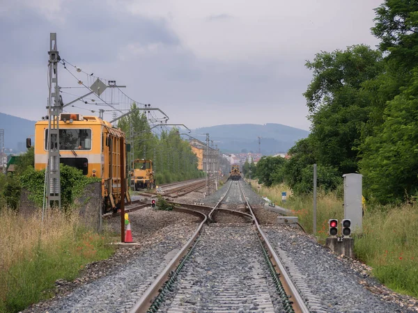 Railway machines on the rails parked on the service tracks waiting to work next to illuminated red signals in a work zone and temporary low tracks at the entrance to Monforte station