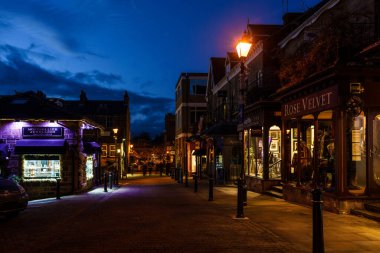 Günbatımında bağımsız dükkanları olan yaya kaldırımlı bir sokak hattı. Arka planda müşteriler, Montpellier Quarter, Harrogate, Kuzey Yorkshire, İngiltere.