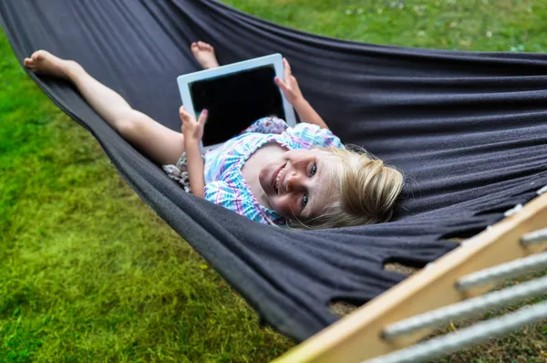 Kind liegt mit Tablet in Hängematte lizenzfreie Stockbilder