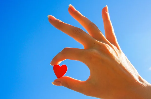 gökyüzünde kırmızı bir kalp tutan kadın eli