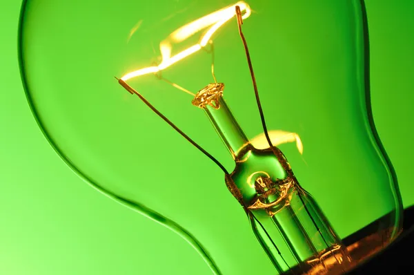 Close up glowing light bulb on green background — Stock Photo, Image
