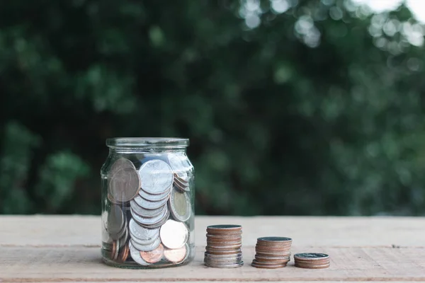 Coins in clear jar placed on wooden planks outdoors in the garden, investment saving concept.copy space.