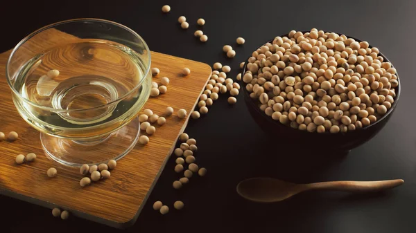 soybean and bowl with oil on a wooden cutting board on black background, front view,selective focus.