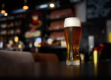 Glass of beer on a table in a bar on blurred bokeh background clipart