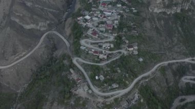 Dağlarda inanılmaz bir yılan var. Virajlı bir yola inşa edilmiş dağlardaki yerleşim yerinin havadan görüntüsü. Dağ manzarası, uzak bölgelerdeki altyapı. Dlog-M 10 bit