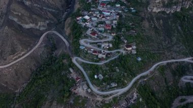 Dağlarda inanılmaz bir yılan var. Virajlı bir yola inşa edilmiş dağlardaki yerleşim yerinin havadan görüntüsü. Dağ manzarası, uzak bölgelerdeki altyapı. 10 bit Video