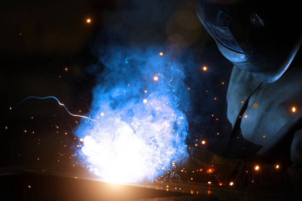 Welder at work. Welding of metal sparks and smoke in the workshop. Industrial Welder With gas Torch in Protective Helmet, welding metal profiles. The welding operation at construction site
