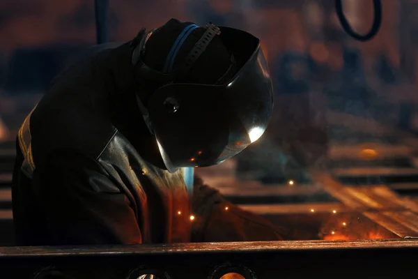 Soldador en el trabajo. Soldadura de chispas metálicas y humo en el taller. Soldador industrial con antorcha de gas en casco protector, soldadura de perfiles metálicos. La operación de soldadura en el sitio de construcción —  Fotos de Stock