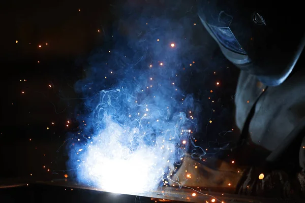 Saldatore al lavoro. Saldatura di scintille metalliche e fumo in officina. Saldatore industriale con torcia a gas nel casco protettivo, profili metallici di saldatura. L'operazione di saldatura in cantiere — Foto Stock