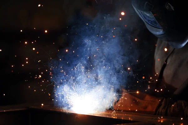 Saldatore al lavoro. Saldatura di scintille metalliche e fumo in officina. Saldatore industriale con torcia a gas nel casco protettivo, profili metallici di saldatura. L'operazione di saldatura in cantiere — Foto Stock