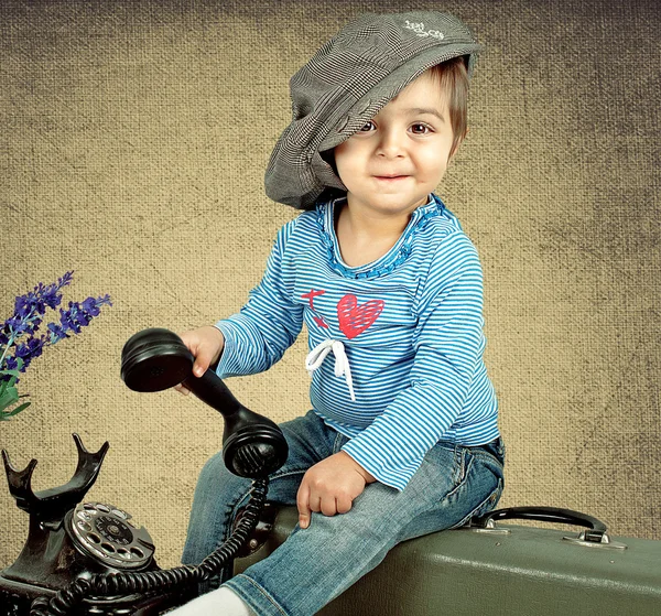 Chica en una gorra se sienta en una maleta — Foto de Stock