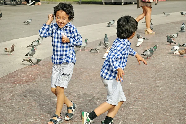 Boys playing on the square with pigeons — Stock Photo, Image