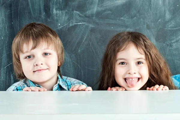 Boy and girl hiding behind a table near the school board — Stock Photo, Image