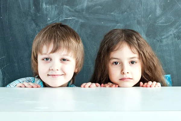 Junge und Mädchen verstecken sich hinter einem Tisch in der Nähe der Schultafel Stockfoto