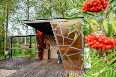 Mangal ızgarası, masa ve sandalyeli piknik alanı. Kırmızı dağ külleri ön planda..