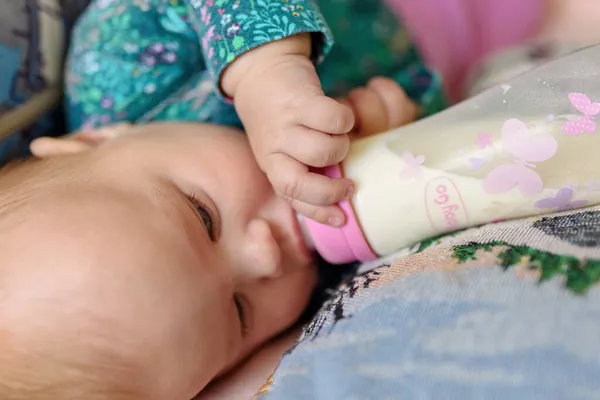 3ヶ月の少女は瓶からミルクを飲む ストックフォト