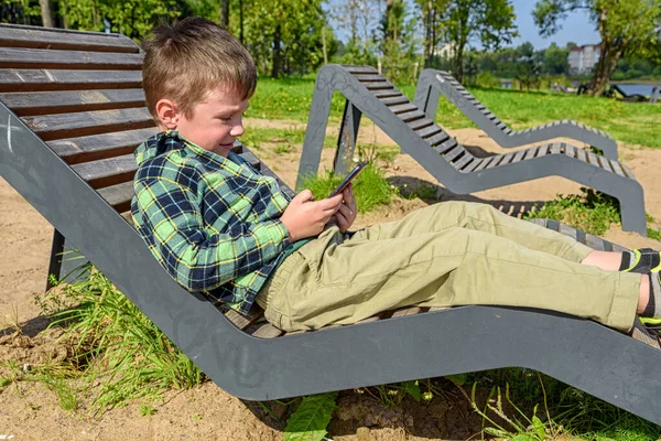 Gelukkig Jongetje Zit Een Bankje Speelt Een Mobiele Telefoon Tegen — Stockfoto