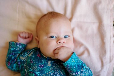 Üç aylık bebek yatakta uzanıyor ve kalemini emiyor.