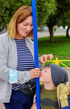 Beş yaşında sevimli bir çocuk, açık havada çocuk parkında sallanıyor. Çocuk parkında anne ile oğul arasındaki iletişim.