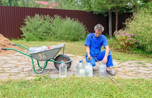 Человек Синем Комбинезоне Наливает Питьевую Воду Шланга Большие Бутылки Экологически — стоковое фото