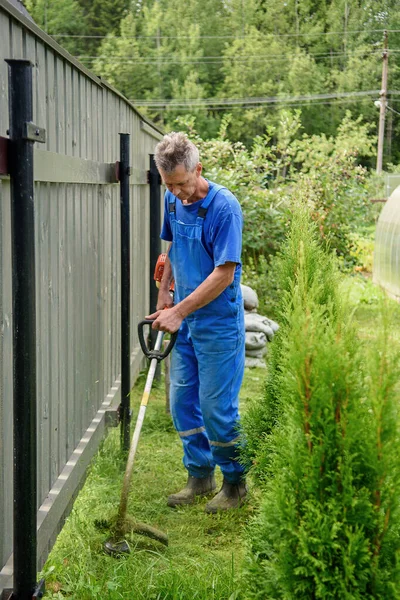 彼の手に手のトリマーを持つ労働者は家の前に草を刈る トリマーは男の手にある 庭師は草を切る ライフスタイル — ストック写真