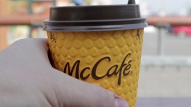 Bir adamın eli, McCafe 'nin sarı kağıt bardağına kahve koyar. Paket yemek. Bir adam McDonald 's fast food restoranında sıcak kahve ya da çay içer. Ağır çekim. Ukrayna, Kiev - 12 Eylül 2021.