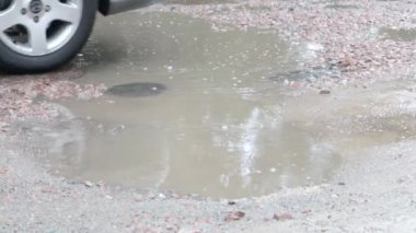 Yoldan geçen arabalarla dolu asfalt bir yolda su dolu çukurlar. Yağmurlu bir hava. Araba, gün içinde yağmurdan sonra asfalt yollardaki su birikintilerinden geçiyor. Yağmur damlaları ve arabalar yolda.