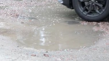 Yoldan geçen arabalarla dolu asfalt bir yolda su dolu çukurlar. Yağmurlu bir hava. Araba, gün içinde yağmurdan sonra asfalt yollardaki su birikintilerinden geçiyor. Yağmur damlaları ve arabalar yolda.