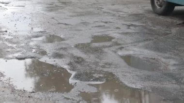 Yoldan geçen arabalarla dolu asfalt bir yolda su dolu çukurlar. Yağmurlu bir hava. Araba, gün içinde yağmurdan sonra asfalt yollardaki su birikintilerinden geçiyor. Yağmur damlaları ve arabalar yolda.