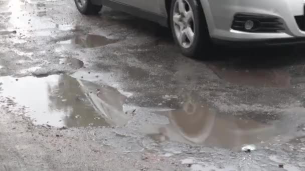 沥青路面上的注满水的坑洞里有过往的汽车 白天下雨后 汽车在破烂不堪的柏油路上穿过水坑 道路上的雨点和车辆 — 图库视频影像