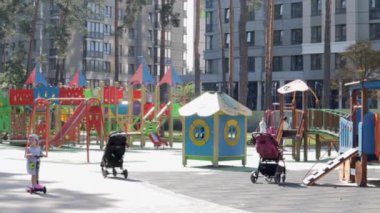 Parktaki bahçedeki renkli, modern çocuk parkında, rahatlatıcı ve oyuncu çocuklar var. Yeşil ağaçlar ve yeni evlerle çevrili bir parkta oyun parkı. Ukrayna, Kyiv - 29 Haziran 2021.