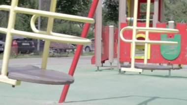 Biri boş, insansız, metal sarısı salıncak açık hava salıncaklarında konut binalarının avlusunda, ileri geri hareket ediyor. Çocuklar için serbest atış. Ukrayna, Kyiv - 29 Haziran 2021.