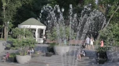 Harkov 'daki Shevchenko parkındaki çeşmeler. Şehir merkezinde halka açık bir çeşme, güneşli bir parkta su püskürtme, insanlar parkta yürüyüp rahatlıyor. Ukrayna, Harkiv - 17 Temmuz 2021.