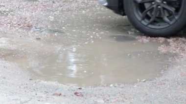 Yoldan geçen arabalarla dolu asfalt bir yolda su dolu çukurlar. Yağmurlu bir hava. Araba, gün içinde yağmurdan sonra asfalt yollardaki su birikintilerinden geçiyor. Yağmur damlaları ve arabalar yolda.