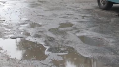 Yoldan geçen arabalarla dolu asfalt bir yolda su dolu çukurlar. Yağmurlu bir hava. Araba, gün içinde yağmurdan sonra asfalt yollardaki su birikintilerinden geçiyor. Yağmur damlaları ve arabalar yolda.