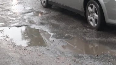 Yoldan geçen arabalarla dolu asfalt bir yolda su dolu çukurlar. Yağmurlu bir hava. Araba, gün içinde yağmurdan sonra asfalt yollardaki su birikintilerinden geçiyor. Yağmur damlaları ve arabalar yolda.