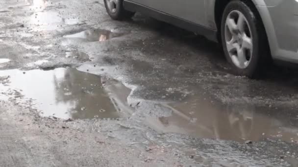沥青路面上的注满水的坑洞里有过往的汽车 白天下雨后 汽车在破烂不堪的柏油路上穿过水坑 道路上的雨点和车辆 — 图库视频影像