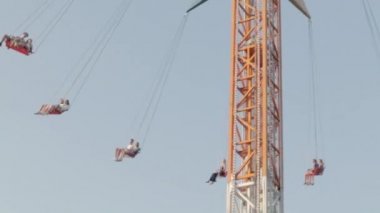Eğlence parkında yüksek atlıkarıncaya bin. İnsanlar yüksek bir zincirle salıncakta sallanırken eğlenirler, mavi gökyüzüne karşı sürüşün tadını çıkarırlar. Ukrayna, Harkiv - 17 Temmuz 2021.
