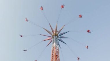 Eğlence parkında yüksek atlıkarıncaya bin. İnsanlar yüksek bir zincirle salıncakta sallanırken eğlenirler, mavi gökyüzüne karşı sürüşün tadını çıkarırlar. Ukrayna, Harkiv - 17 Temmuz 2021.