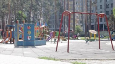 Bahçedeki modern çocuk parkında rahatlatıcı ve oyuncu çocuklar var. Zaman ayarlı. Yeşil ağaçlar ve yeni evlerle çevrili bir parkta oyun alanı.