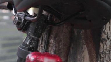 Bisiklet kırmızı yanıp sönen LED stop lambası. Kırmızı ışık görüntüleriyle bir ağacın yakınına park edilmiş bir velomotorun arkası. Bisiklet teşhircisi çalışıyor.