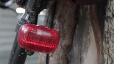 Bisiklet kırmızı yanıp sönen LED stop lambası. Kırmızı ışık görüntüleriyle bir ağacın yakınına park edilmiş bir velomotorun arkası. Bisiklet teşhircisi çalışıyor.